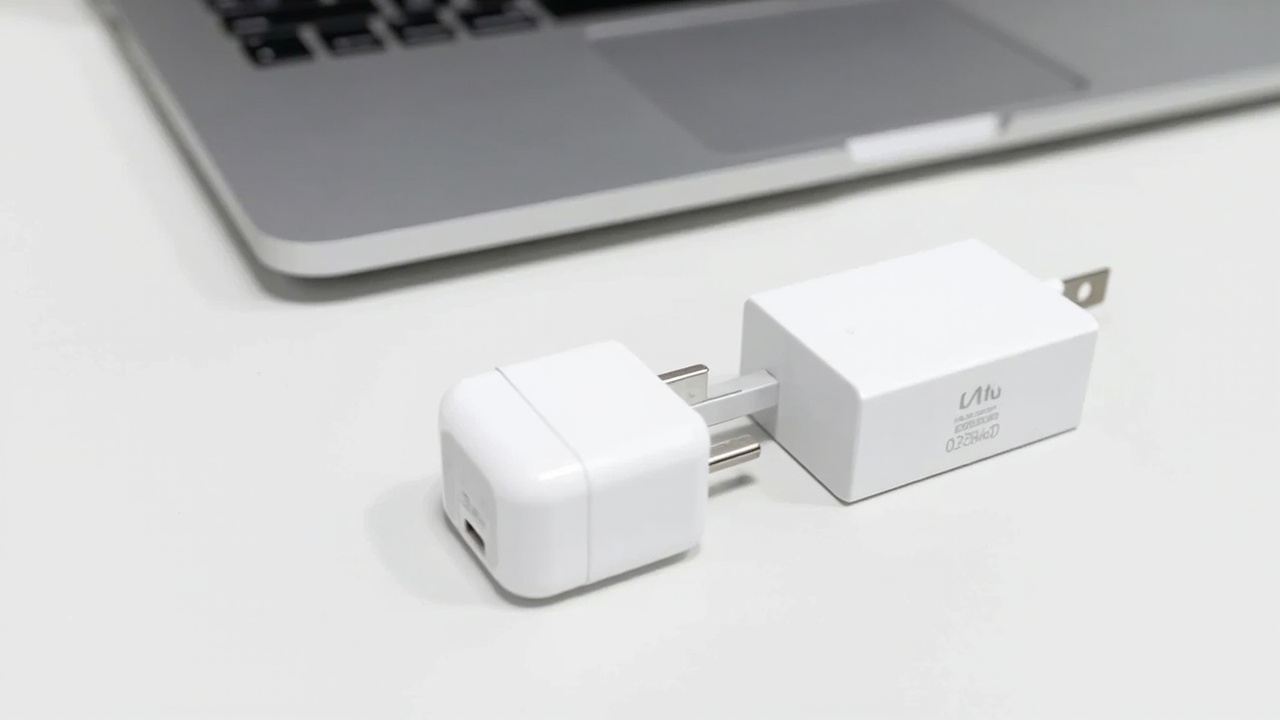Two chargers side by side with a MacBook Pro on a clean white surface, overhead view